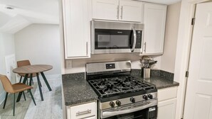 Cocina compacta con estufa a gas, microondas y horno. Hay una mesa de comedor con sillas y una alfombra pequeña.