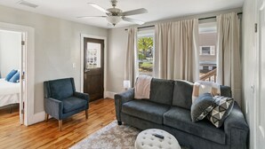 A living room with a dark gray sofa, a blue armchair, a round ottoman, and a ceiling fan. - Cozy Spot in Heart of Libertyville Near Naval Base (Libertyville)