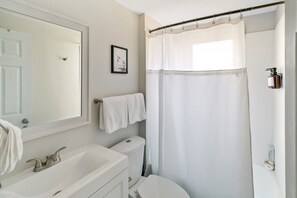 A bathroom with a white sink, mirror, and toilet. There is a towel hanging on the wall and a shower curtain.
