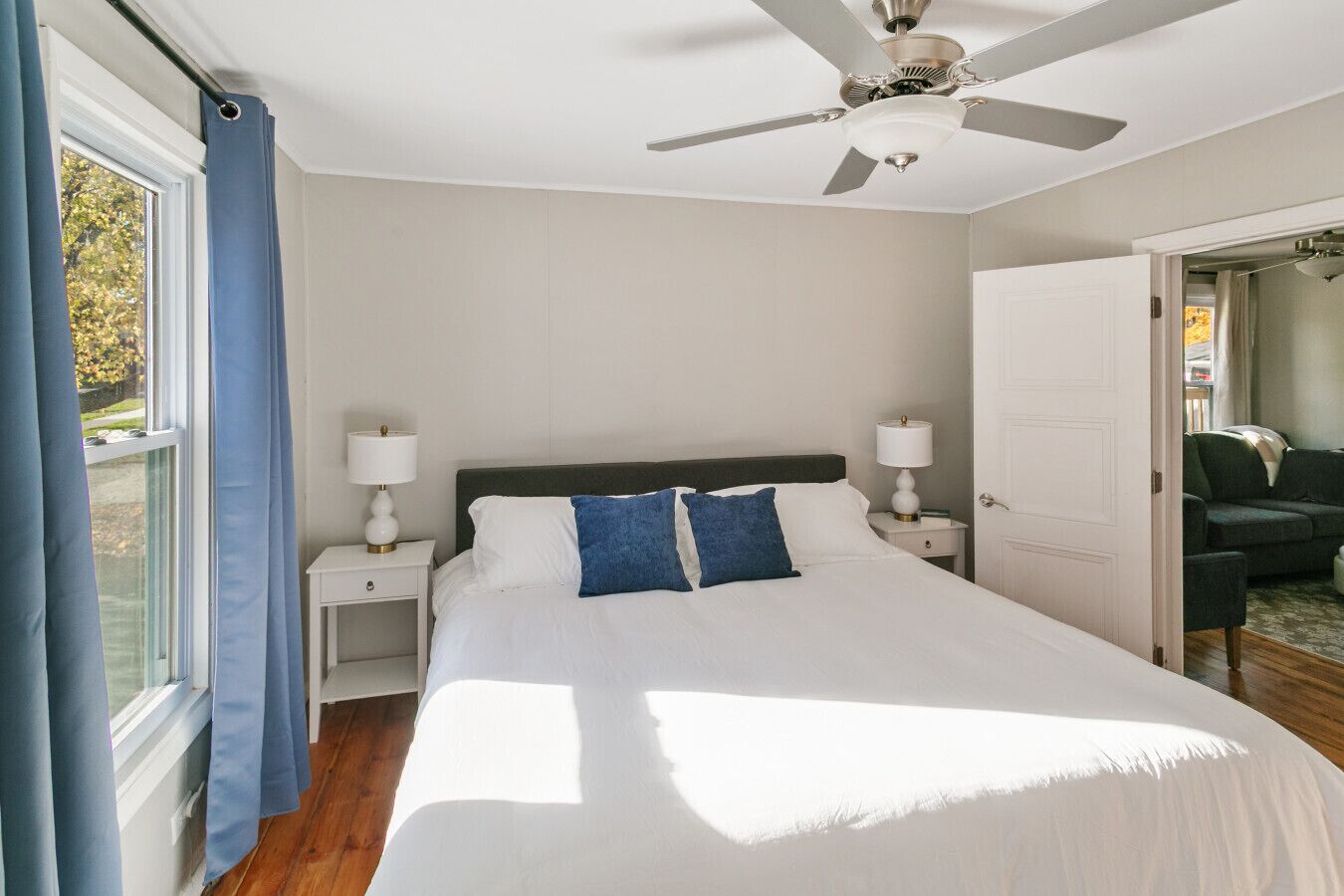 A bedroom with a bed, two bedside tables, a ceiling fan, and a door leading to another room.