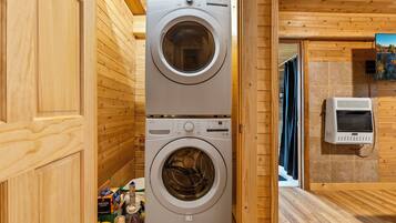 Une buanderie équipée de deux machines à laver superposées, d’un sèche-linge et d’un mur carrelé orné d’un tableau.