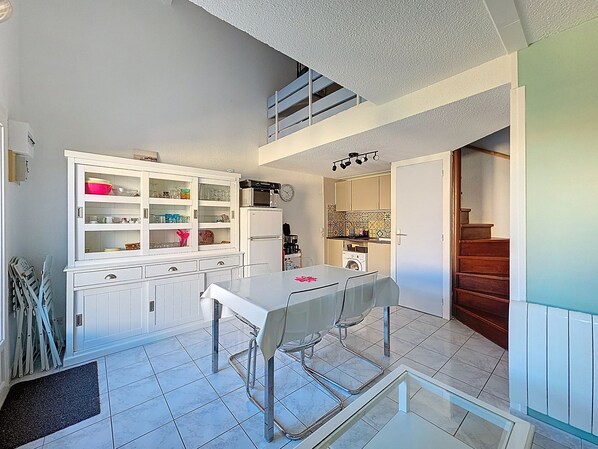 Cocina compacta con armarios blancos, una mesa de comedor con sillas, un microondas y una lavadora.