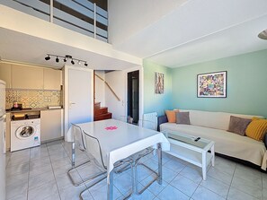 A compact living space with a dining area, kitchenette, washing machine, staircase, and a sofa with cushions.