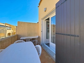 Varanda com mesa e cadeiras brancas, porta de correr de vidro e parede com textura.