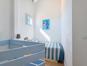 Ein Zimmer mit zwei Betten, einem kleinen Tisch mit Lampe, einem Bild an der Wand und einem Fenster, das natürliches Licht hereinlässt.