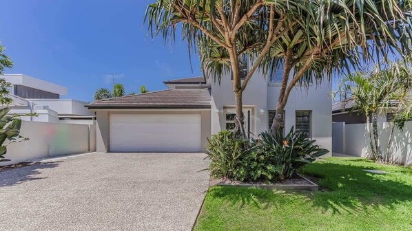 A modern two-story house with a garage, a well-maintained lawn, and a palm tree.