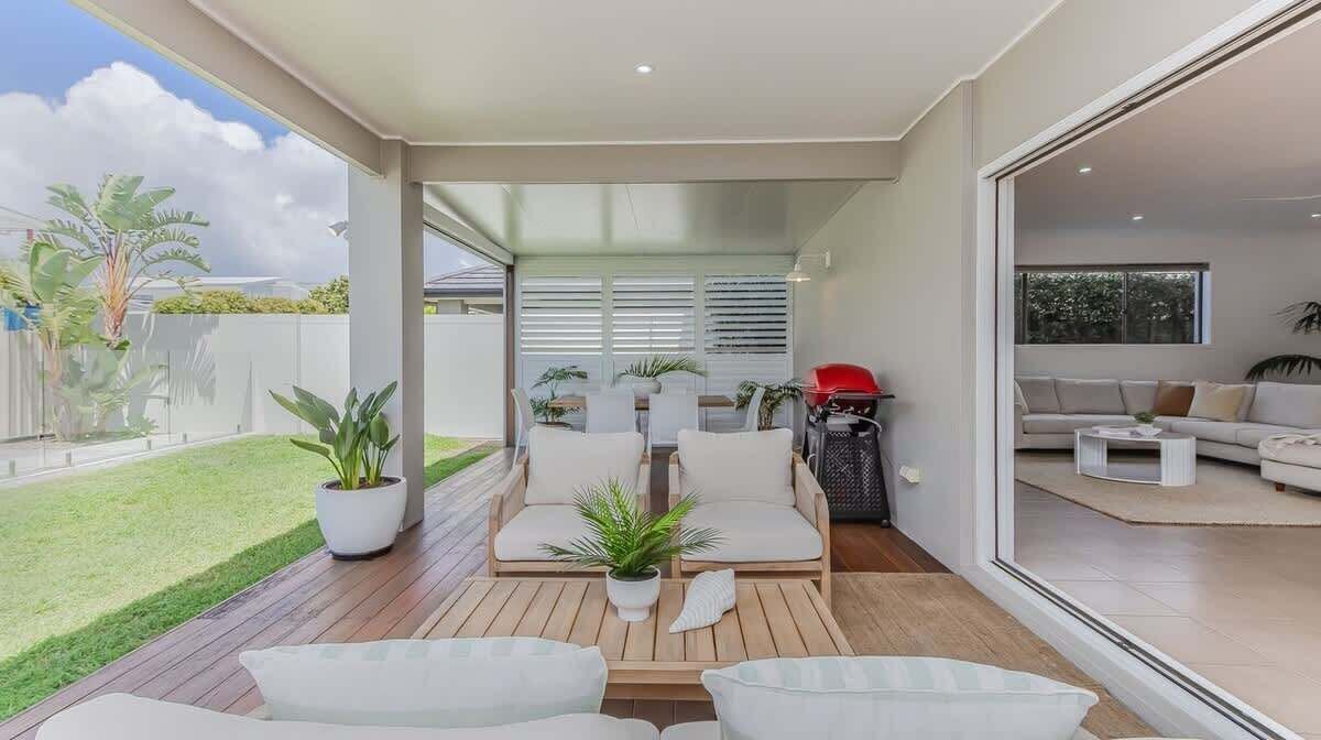 A modern outdoor living area with a wooden deck, white furniture, and potted plants.