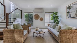 A modern living room with wicker furniture, a central coffee table, and a staircase with glass railings.