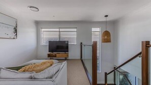 A modern bedroom with a sofa, TV, and a glass railing leading to a balcony.