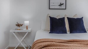 A bedroom with a bed, pillows, a bedside table with a lamp, and a framed picture on the wall.