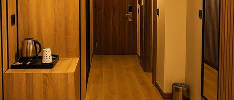 Een hotelkamer met een groot bed, een houten kledingkast, een kleine tafel met waterkoker en beker, en een prullenbak.