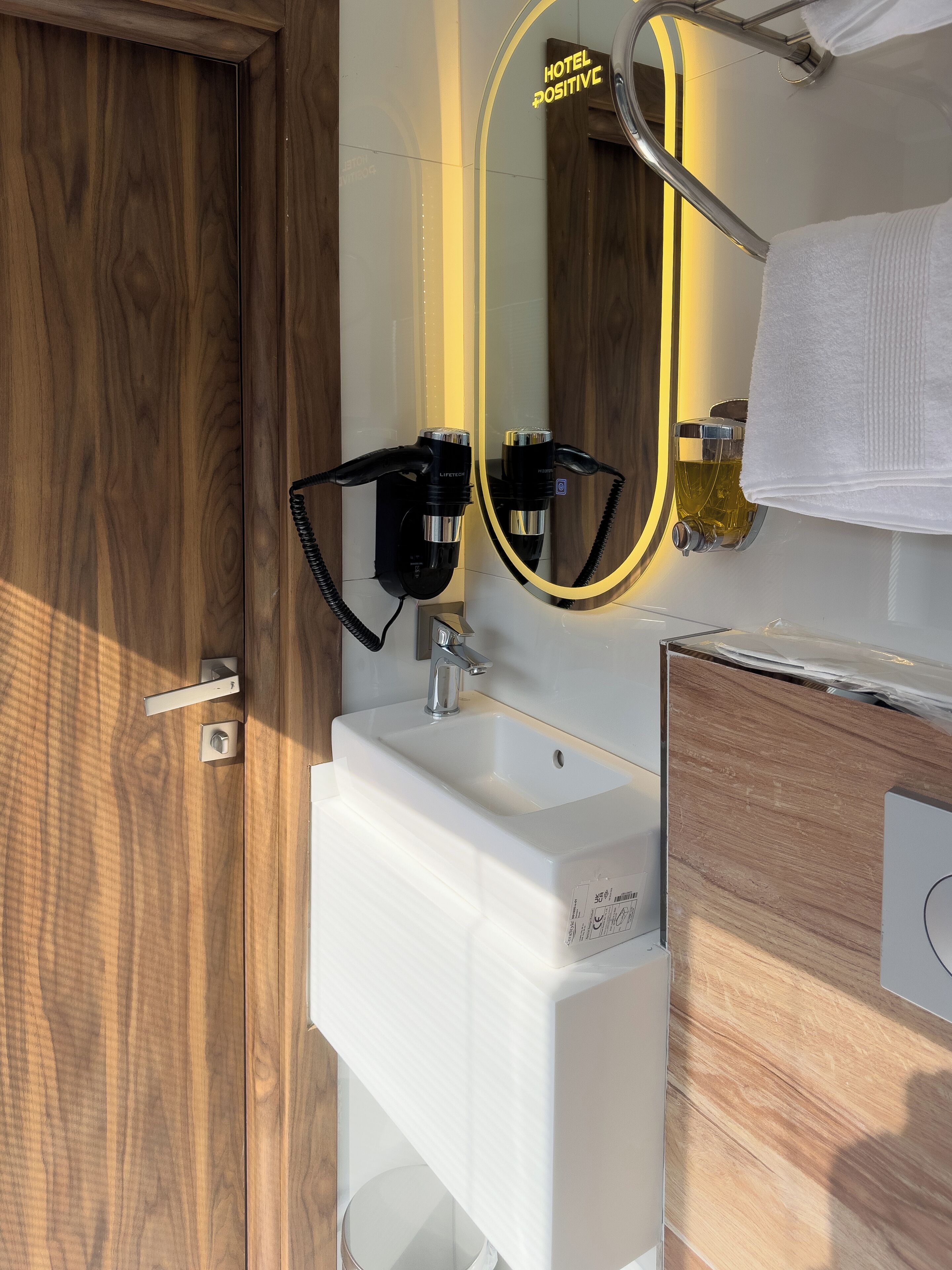 A bathroom with a white sink, a mirror with a yellow frame, a towel hanging on a rack, and a wooden door.