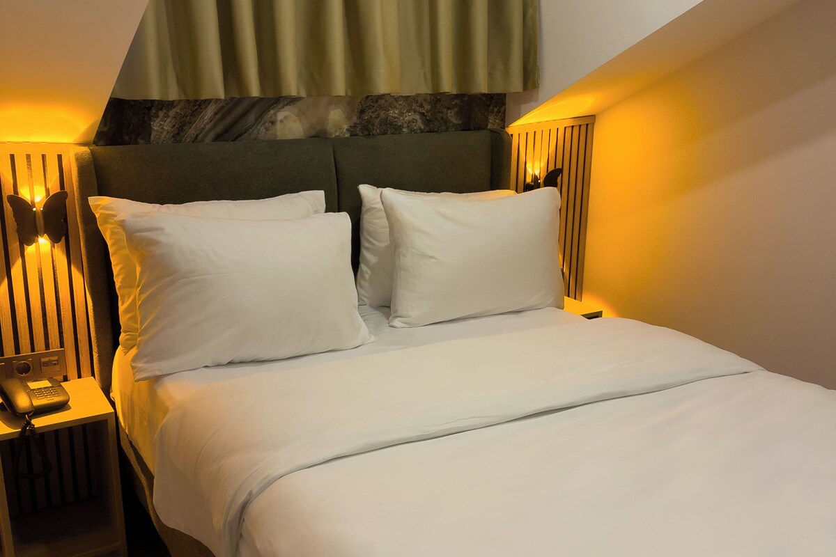A neatly made bed with white linens, a bedside lamp, and a telephone on the nightstand.