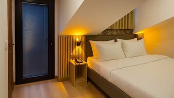 A hotel room with a bed, bedside table, lamp, and a door with blinds.