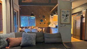 A modern living room with a black leather sofa, a wooden ceiling, and a dining area in the background. - NEW & FUN! Hot Tub, EV Outlet in Garage (Mammoth Lakes)
