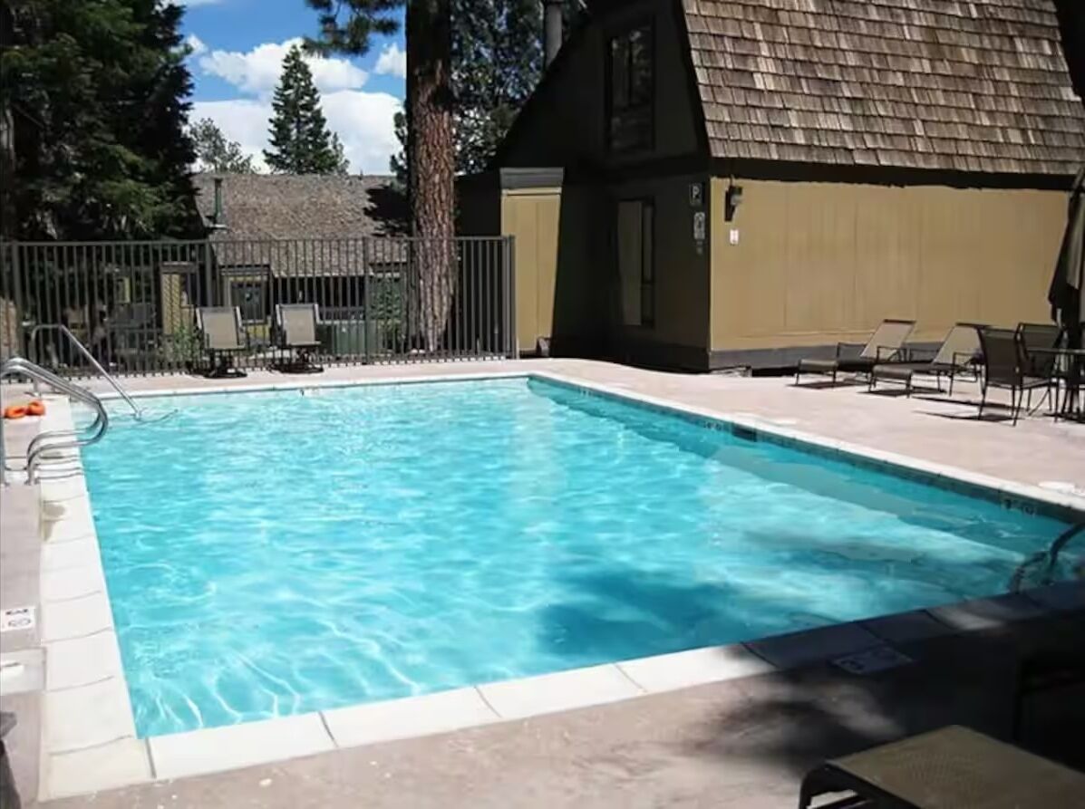 En rektangulär swimmingpool med klart, blått vatten, omgiven av en kakelbeklädd poolterrass och ett staket.