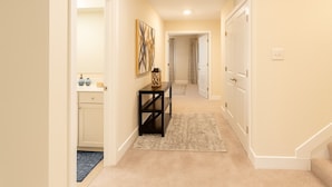 A hallway with a carpeted floor, a console table with decorative items, and a door leading to another room. - Lux Escape w/King Bed/Loft/Skyline Views near BLT (Woodlawn)