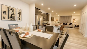 A modern dining area with a dark wooden table, white placemats, and matching chairs. A kitchen with stainless steel appliances is visible in the background. - Lux Escape w/King Bed/Loft/Skyline Views near BLT (Woodlawn)