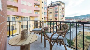 Un balcon avec des fauteuils et une table en osier, donnant sur une rue et des immeubles.