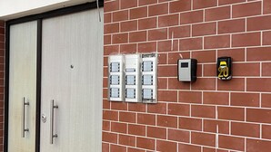 Un mur de briques avec un détecteur d’incendie, une porte en métal avec des poignées et une fenêtre avec un cadre en métal.