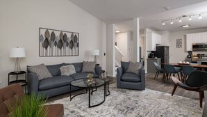 Un salon moderne avec un canapé gris, une table basse et un coin repas comprenant une table et des chaises en bois.
