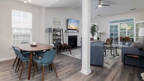 Un salon spacieux avec une cheminée, un coin repas avec une table ronde et des chaises, et un espace détente avec un canapé et des fauteuils.