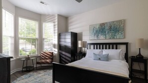 Une chambre à coucher avec un lit, une chaise, une armoire, un tableau et une fenêtre avec des stores.