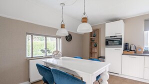 A modern kitchen with white cabinets, a built-in oven, and a coffee maker. - Charming Villa Near the sea and Forest (De Koog)