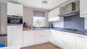A modern kitchen with white cabinets, a built-in oven, a gas stove, and a window providing natural light. - Charming Villa Near the sea and Forest (De Koog)