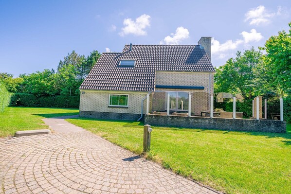A two-story house with a tiled roof, a paved driveway, and a well-maintained lawn. - Charming Villa Near the sea and Forest (De Koog)