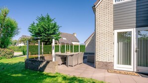 A patio with a table and chairs, a brick wall, and a sliding glass door. - Charming Villa Near the sea and Forest (De Koog)