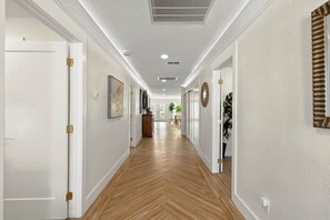 Un couloir doté d’un plancher en bois, de murs blancs et de portes avec des poignées en laiton.