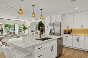 A modern kitchen with white cabinetry, a stainless steel refrigerator, and a large island with a sink. - Constellation Vacation (South Padre Island)