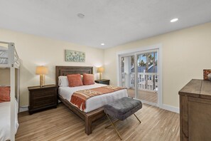A bedroom with a bed, nightstands, a bench, a window with a view, and a door leading to a balcony. - Constellation Vacation (South Padre Island)