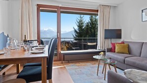 A modern hotel room with a dining area, a sofa, and a TV. - Crans-Montana, 5 pers : balcon vue & parking privé (Crans-Montana)