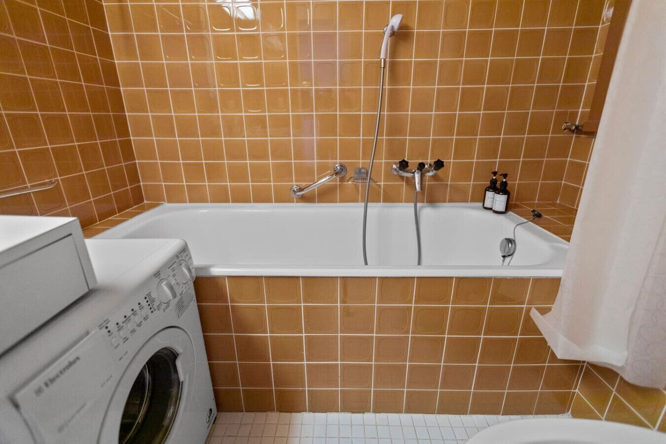 A bathroom with a bathtub, a washing machine, and tiled walls.