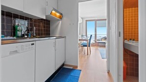 A modern kitchen with white cabinets, a dishwasher, and a blue mat leading to a dining area with a view. - Crans-Montana, 5 pers : balcon vue & parking privé (Crans-Montana)