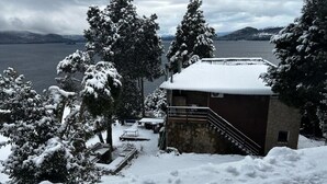 A snow-covered building with a staircase leading to a deck, surrounded by snow-laden trees and a lake in the background. - Upstairs apartment - Seeblick Bariloche (San Carlos de Bariloche)