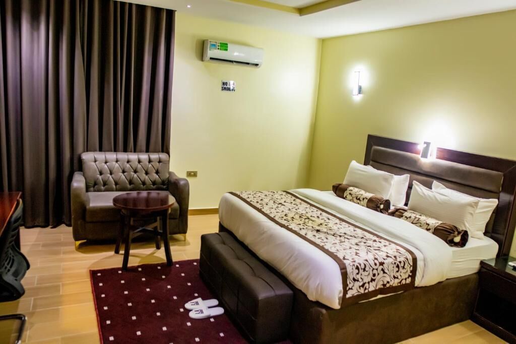 Habitación de hotel con una cama grande, un sofá, una mesita redonda y una alfombra roja con diseños blancos.