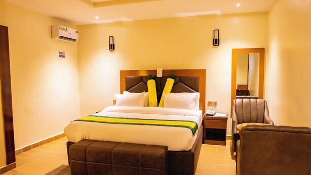 Camera d'albergo con un letto grande, un comodino, una sedia, un condizionatore d'aria e un cartello con scritto “NO SMOKING”.