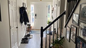 Ein Korridor mit Holzboden, einer Treppe mit schwarzen Geländern und einer Tür am Ende.