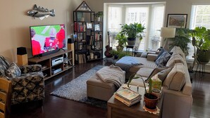 Ein Wohnzimmer mit einem Flachbildfernseher, einem Bücherregal, einer Gitarre, einem Sofa und einem Couchtisch.