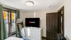 A bedroom with a bed, a dresser, a television on top, a window with curtains, and a door. - Stylish Retreat in DT Libertyville Near Naval Base (Libertyville)