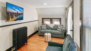 A modern living room with a cityscape painting, a grey sofa, a small ottoman, and a radiator. - Stylish Retreat in DT Libertyville Near Naval Base (Libertyville)