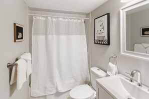 A bathroom with a white toilet, a sink, a shower curtain, and a mirror.