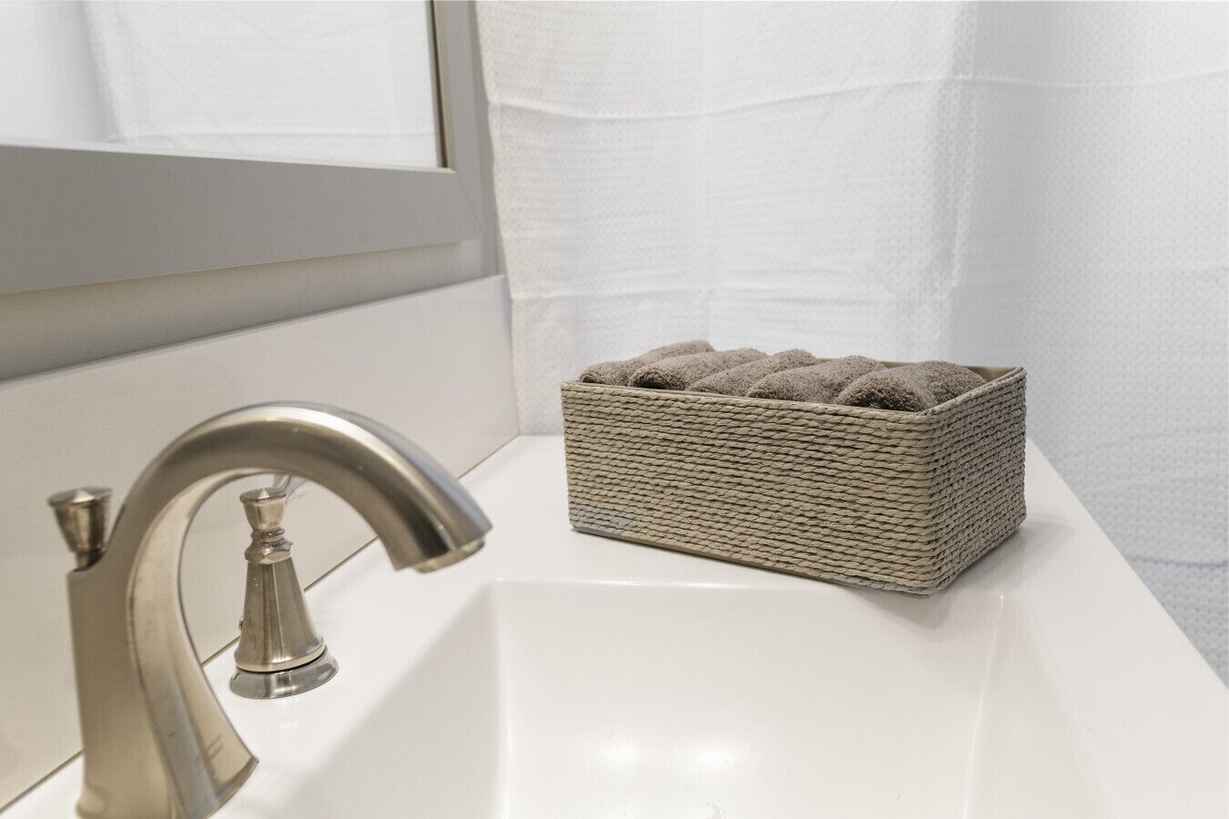 A bathroom with a white sink, a silver faucet, and a woven basket containing rolled towels.