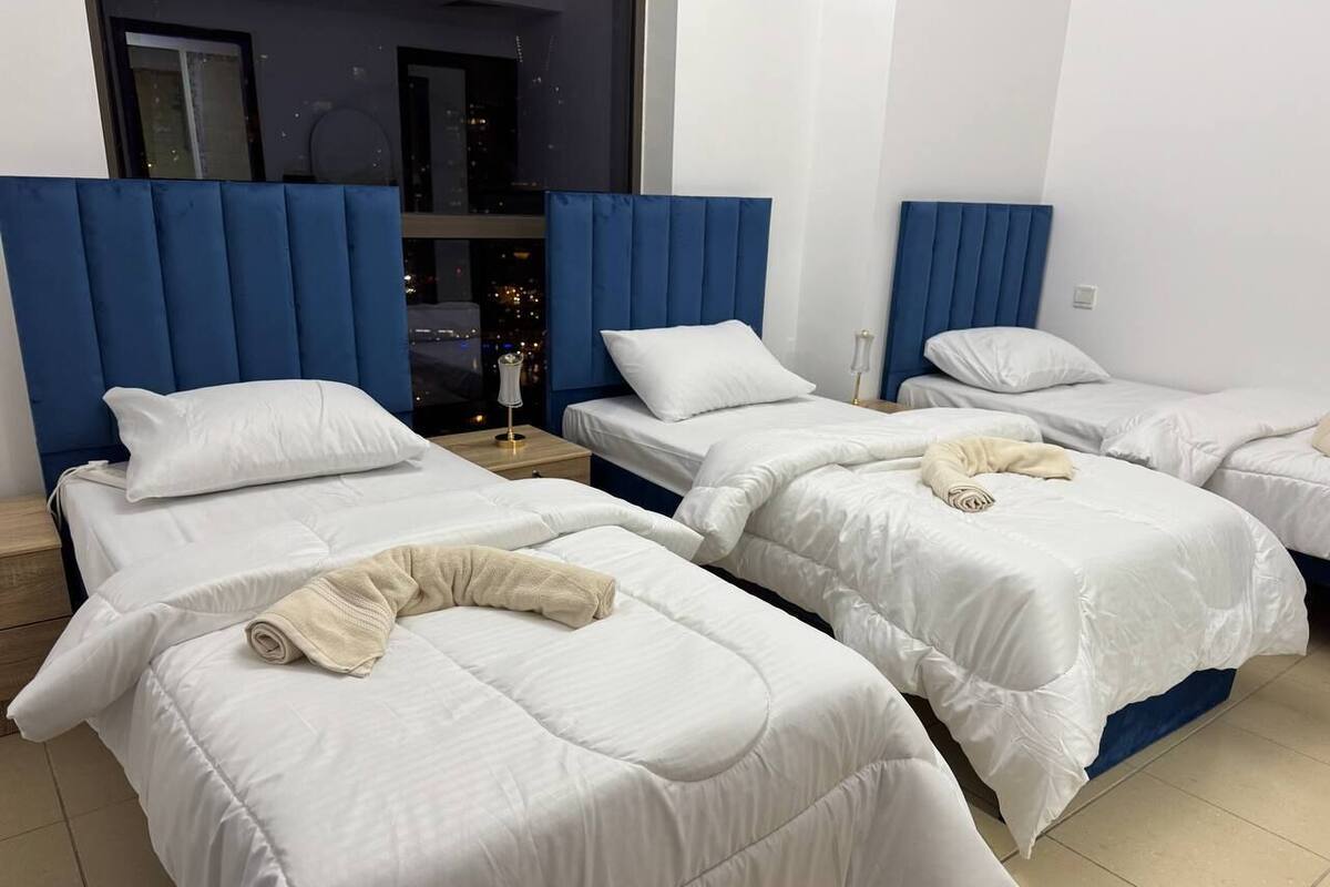 A hotel room with three beds, each with a blue headboard and white bedding.
