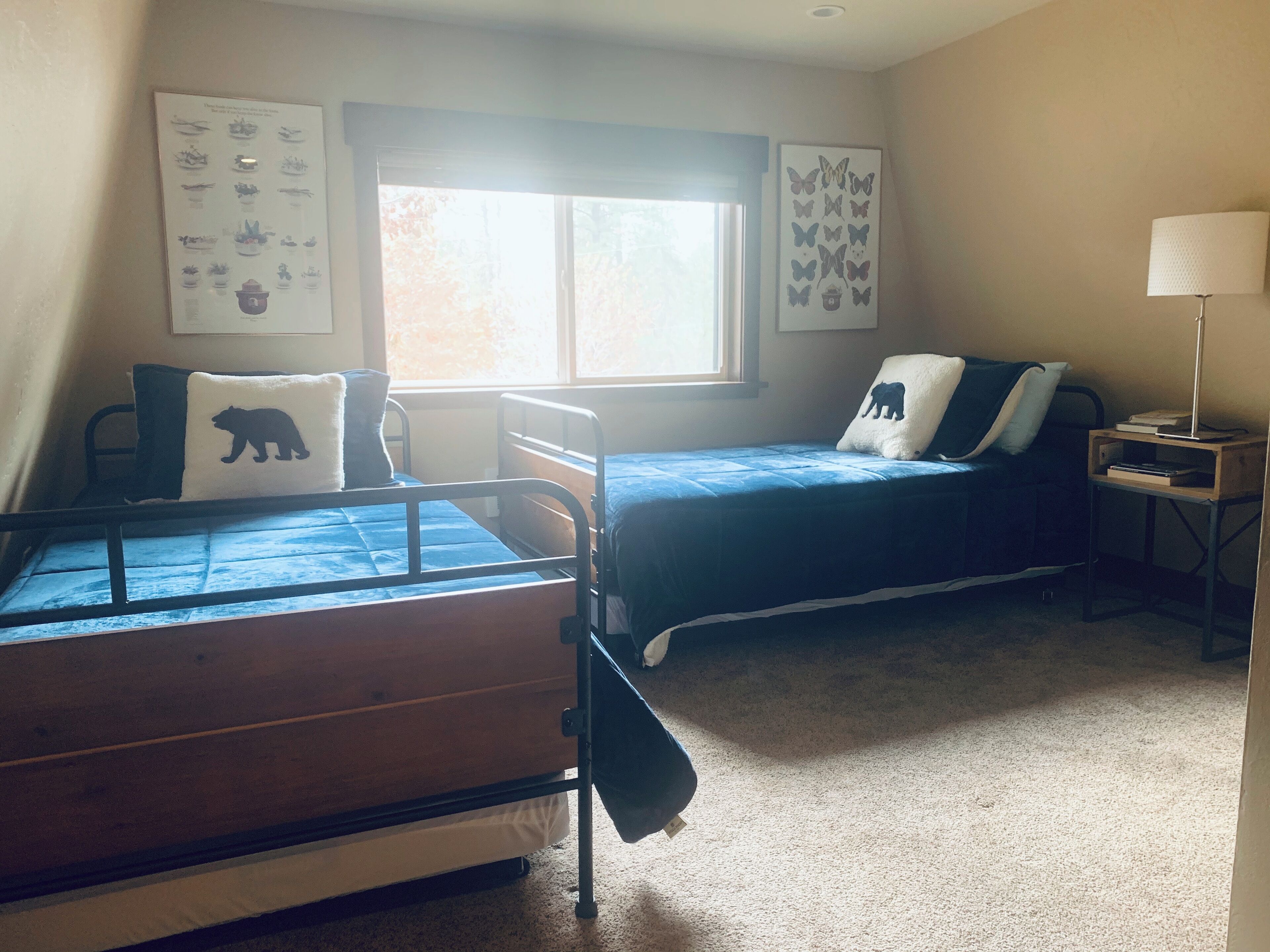 A bedroom with two beds, a window, and a nightstand with a lamp.