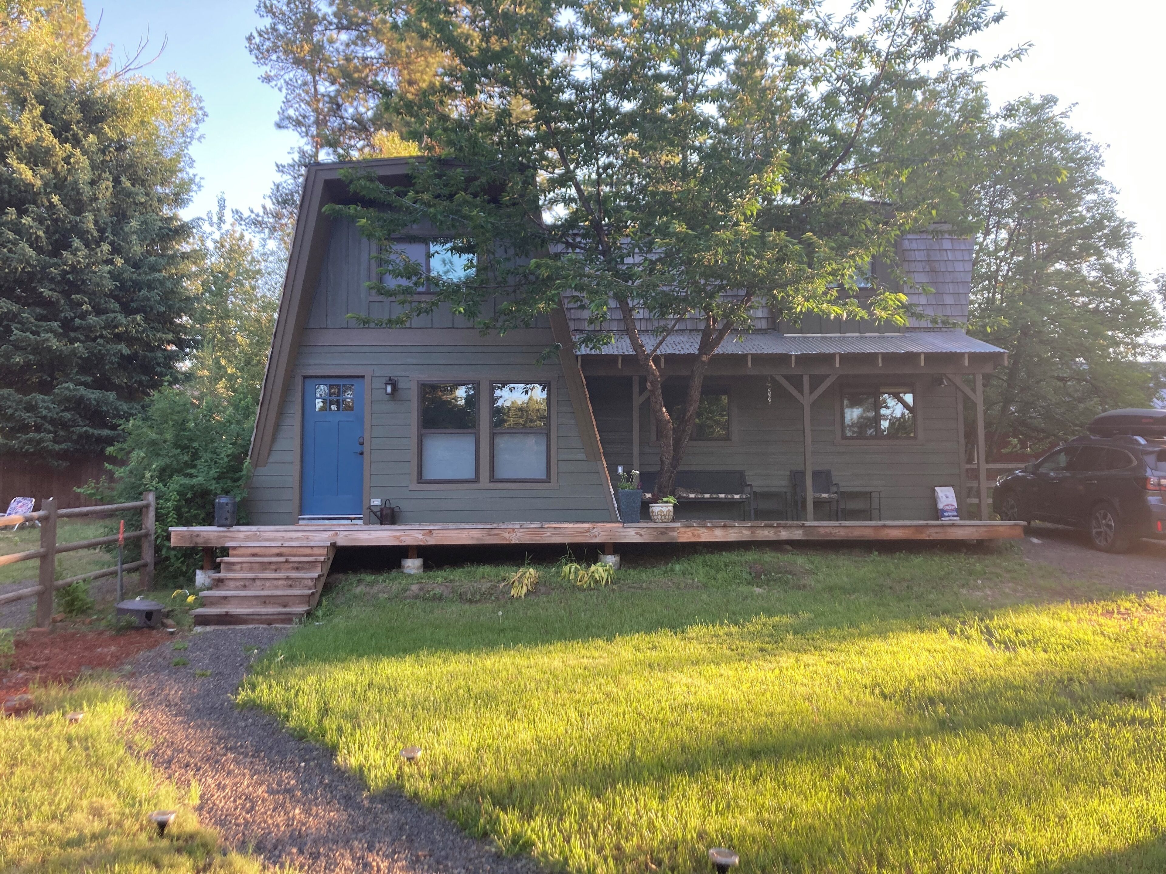A two-story wooden house with a blue door, a deck, and a small garden area.