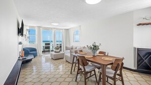 A modern living room with a dining area, large windows, and a fireplace. - Oceanfront Terrace Communal Pool AC (Carolina)